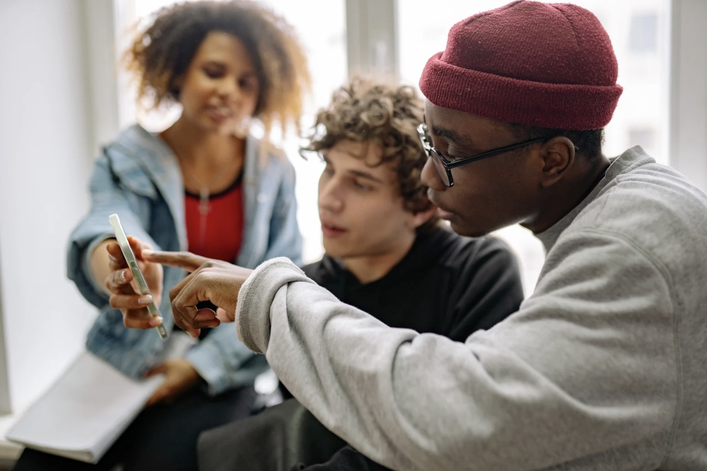 Three young adults sitting together, looking at something on a phone.